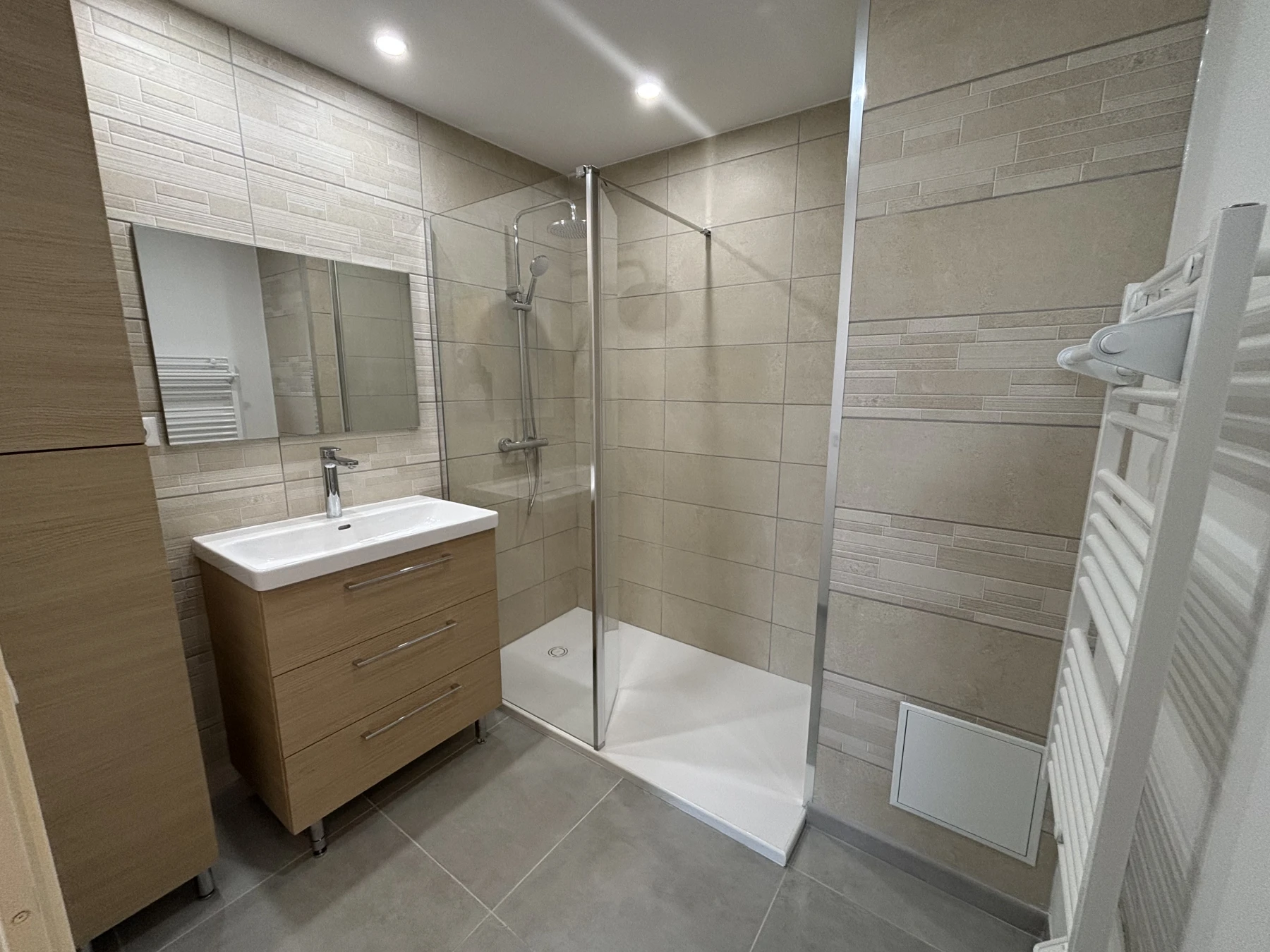 Rénovation complète, dépose de l’ancienne salle de bain, installation d’un faux plafond avec spots, pose d’une chappe maigre, reprise des réseaux d’eaux et d’évacuation, carrelage faïence, pose d’un receveur et de sa paroi vitrée, installation des meubles